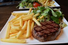 steak and french fries on a white plate with lettuce, tomatoes and tomato