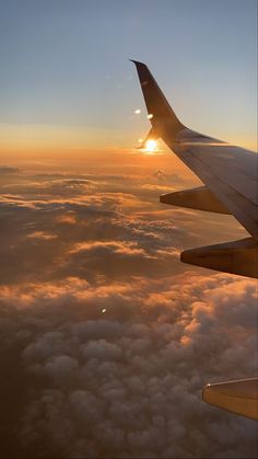 the wing of an airplane as it flies above the clouds at sunset or sunrise, with the sun peeking through the clouds