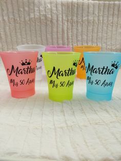 four plastic cups with names on them sitting on a bed in front of a white blanket