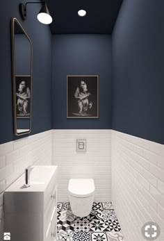 a white toilet sitting next to a sink in a bathroom under two pictures on the wall