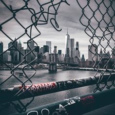 the city skyline is seen through a chain link fence