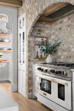 a white stove top oven sitting inside of a kitchen next to a brick wall with an arched doorway