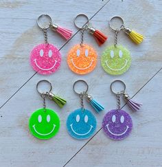 six smiley face keychains with tassels on them, all in different colors