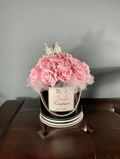 a black hat with pink roses and a tiara on top is sitting on a leather ottoman