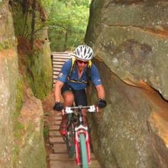 a man riding a bike down a set of stairs in the woods next to large rocks