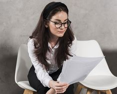 a woman sitting on a chair reading a piece of paper