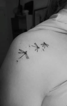 the back of a woman's shoulder with three small dragonflies on her left side