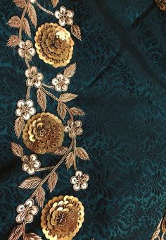 an embroidered fabric with gold flowers and leaves on green background, closeup view from the neck down