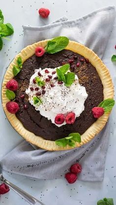 a chocolate pie with raspberries and whipped cream on top, sitting on a table