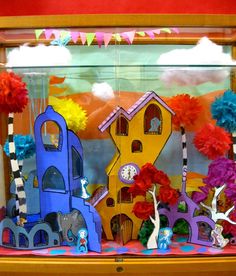 a display case filled with paper cutouts and flowers in front of a window that has colorful decorations on it