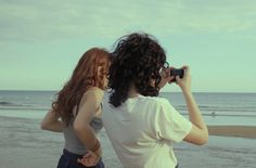 two women are standing on the beach taking pictures