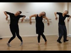 four people in black shirts and pants are dancing on a wooden floor with their arms stretched out