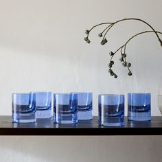 four glasses are lined up on a shelf next to a vase with flowers in it