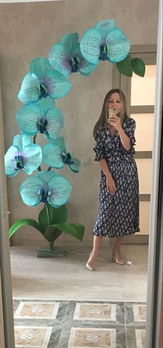 a woman taking a selfie in front of a mirror with flowers on the wall