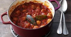 a red pot filled with food next to two silver spoons