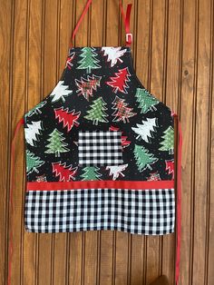 an apron with christmas trees on it hanging from a wooden wall next to a pair of scissors