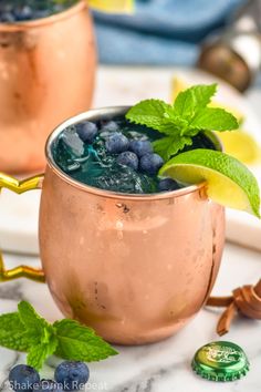 two copper mugs filled with blueberries and mint garnish on a marble table