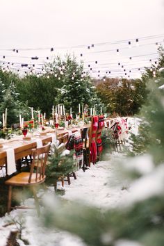 a long table is set up for an outdoor dinner party in the snow with candles and christmas decorations