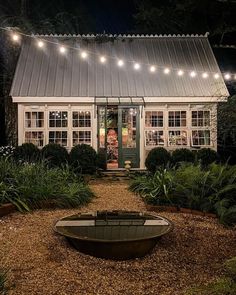 a small white house with lights on the front and side windows, surrounded by greenery