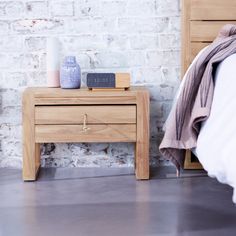 a nightstand with an alarm clock on it next to a bed and a brick wall