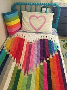 a bed with a rainbow quilt and pillow on it