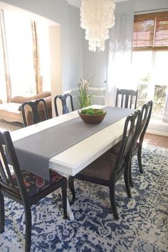 a dining room table with chairs and a bowl on it's centerpiece in front of a window