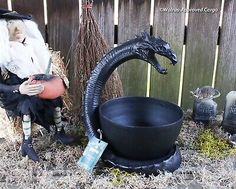 a statue of a witch sitting next to a caulder with a black dragon on it