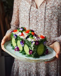 a woman is holding a plate with a cake on it that has cucumbers and flowers on it