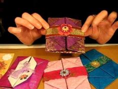 a person is holding up some origami pieces on a table with other folded ones