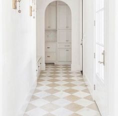 a hallway with white walls and checkered flooring in the middle, leading to an arched doorway