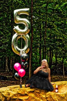 a woman sitting on top of a rock next to balloons and a number 55 sign