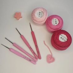 pink crochet hooks, needles and balls of yarn on a white table top