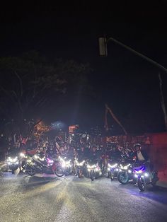 a group of people riding motorcycles down a street at night