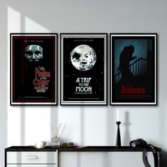 three horror movie posters hanging on the wall above a desk in a room with white walls