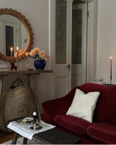 a living room with a red couch, mirror and candles on the table in front of it