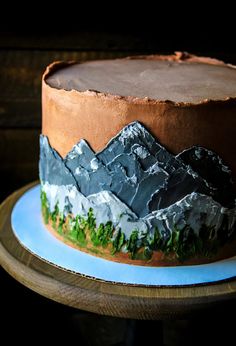 a chocolate cake with mountains on it sitting on a blue and white plate next to a wooden table