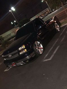 a black truck parked in a parking lot next to a curb with lights on at night