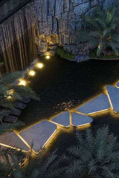 an aerial view of a pool at night with lights in the water and trees surrounding it