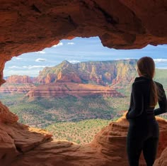 a woman looking out over the canyon from inside a rock formation with mountains in the background