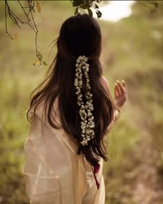 a woman with long hair and flowers in her hair is standing under a tree branch