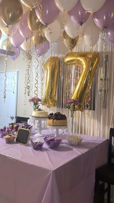 a table topped with balloons and cake next to a number seventy sign hanging from the ceiling