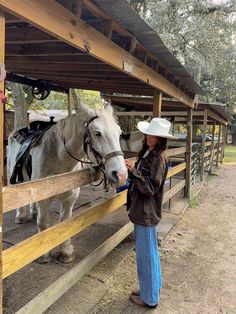 a woman standing next to a white horse in a corral with a cowboy hat on