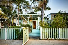 a house with palm trees in front of it and a white picket fence on the sidewalk