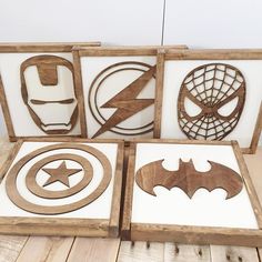 four wooden cut outs with various superhero logos in them on a wood flooring surface