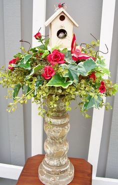 a vase filled with flowers and greenery on top of a wooden table next to a birdhouse