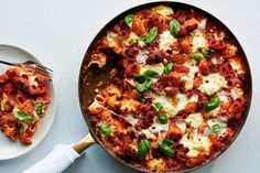 a skillet filled with pasta and sauce next to a plate of food on a table