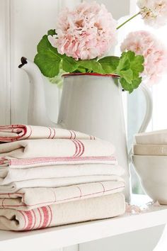 pink flowers are in a white pitcher on a shelf next to folded towels and cups