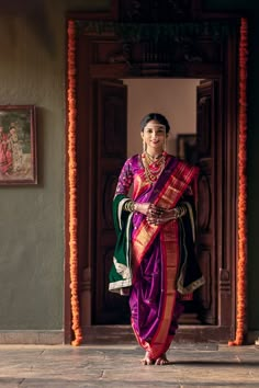 a woman in a purple and green sari is walking into the room with her hand on her hip