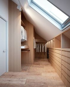 an attic bedroom with wooden closets and skylight in the ceiling, along with white shirts on hangers