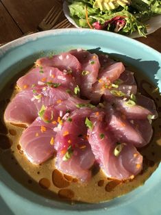 a blue bowl filled with sliced up tuna on top of a table next to a salad